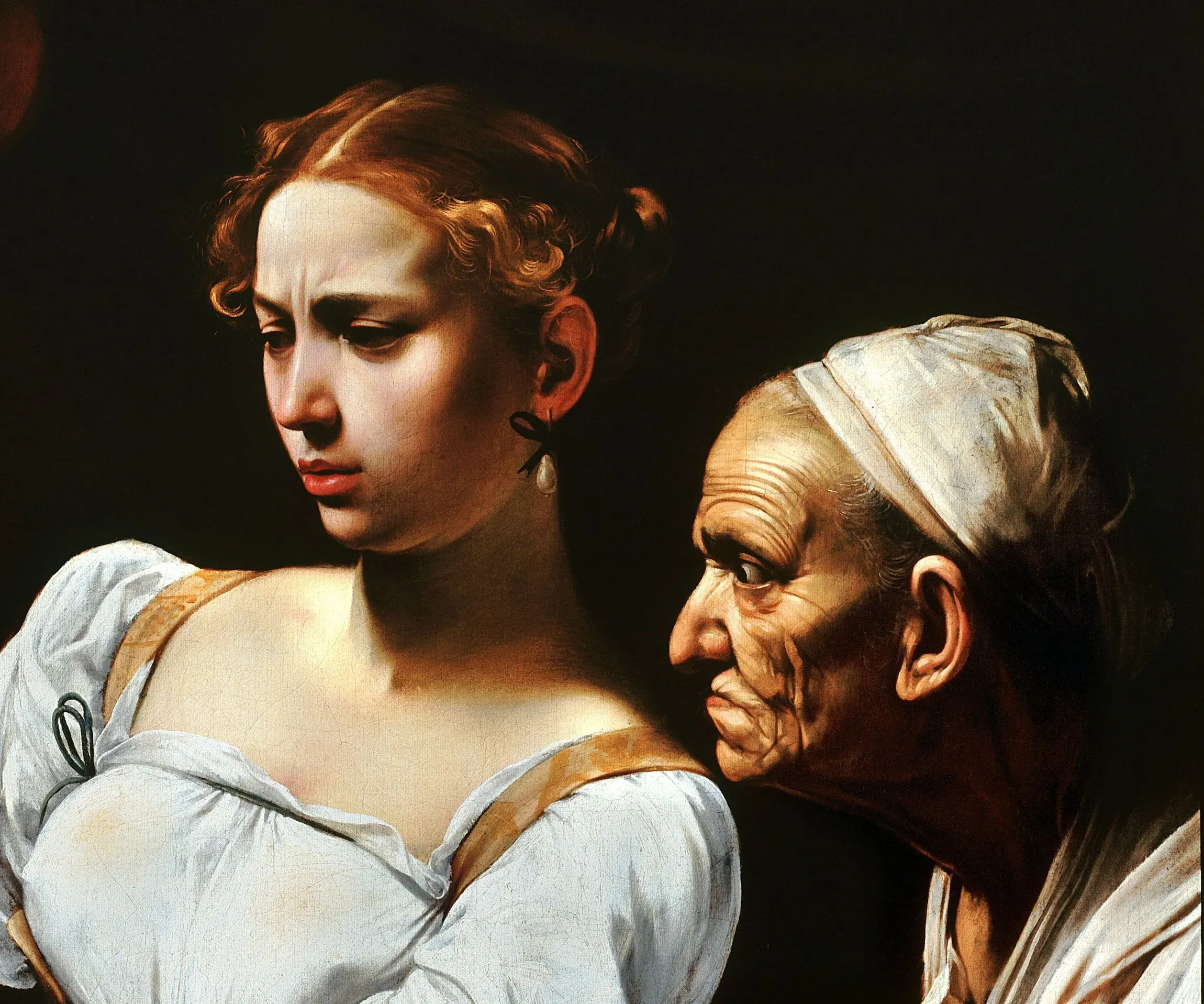 Detail of Judith Beheading Holofernes: two heads lifted out of the black by one hard side light, the young face flinching at what her own hands are doing and the old servant's face beside it, every fold of the skin held in that same light.
