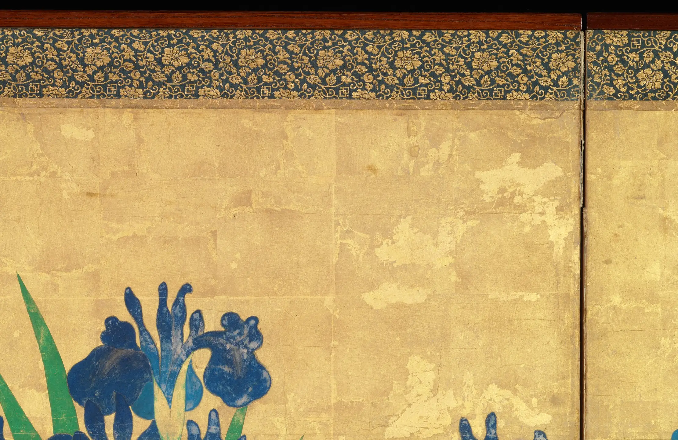 The top of a panel of Irises at Yatsuhashi, where nothing is painted. The ground is gold leaf laid down in squares, and the joins run across the surface in a grid that can be followed from one panel into the next. Where the leaf has worn away the paper underneath shows through as pale cloud. All of this went on first, over the whole screen, before a single iris was put down.