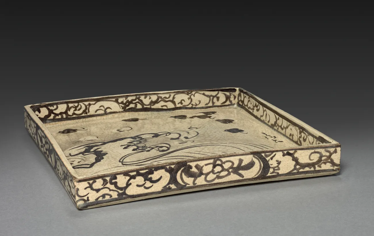 The same dish whole: a square tray with a low wall, made for serving tea cakes. This is not painting on a flat surface. The design runs across the floor of the tray and up the inside of the rim, and it has to hold together seen from above, at a table, with food sitting on it.