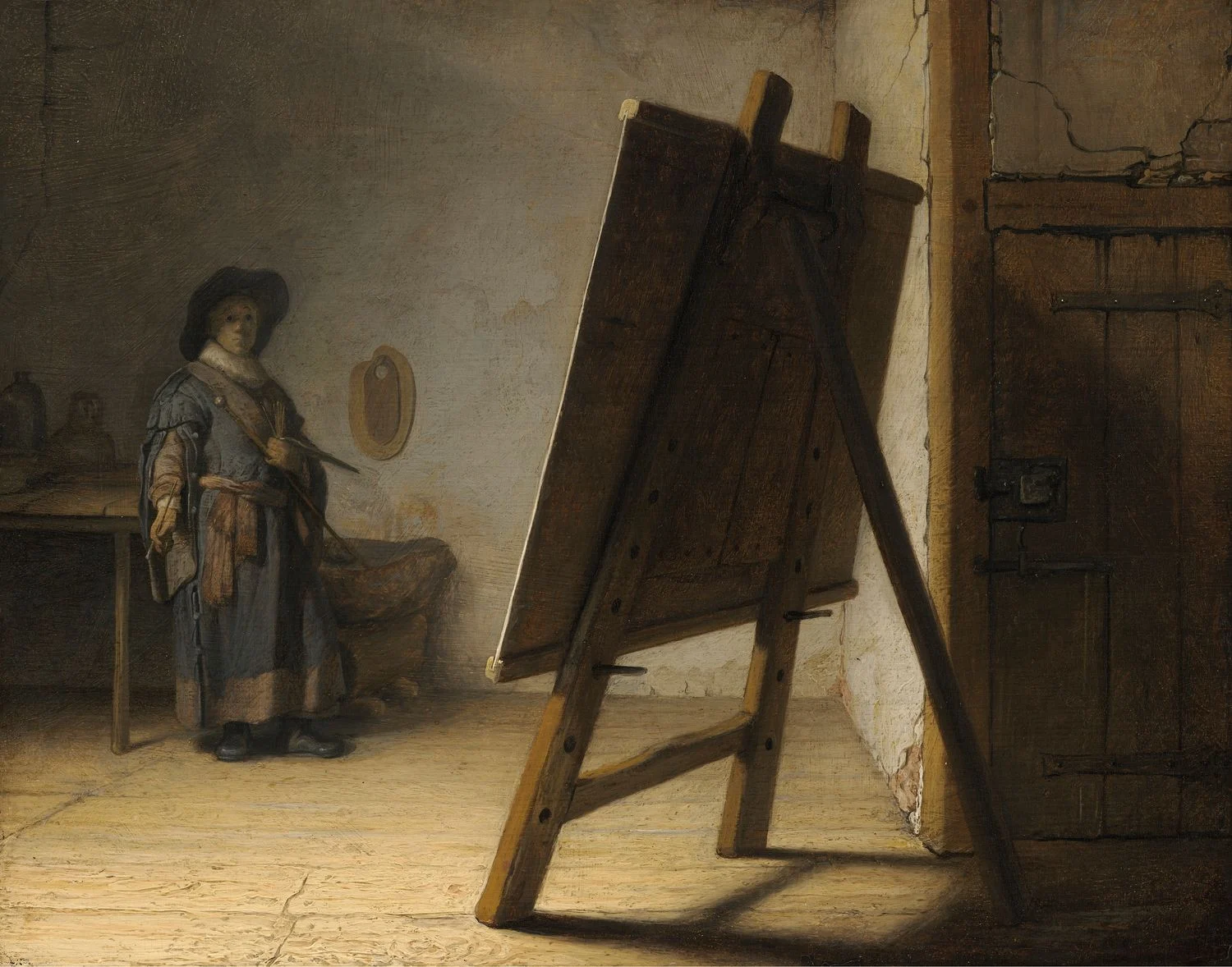 The Artist in his Studio, from the Leiden years: a bare room with cracked plaster, jars on a table at the left, a second palette hanging on the wall and a heavy stone slab on a stand. The panel on the easel is turned away from us and the painter has walked back to the far wall to look at it, which is the actual subject of the picture.