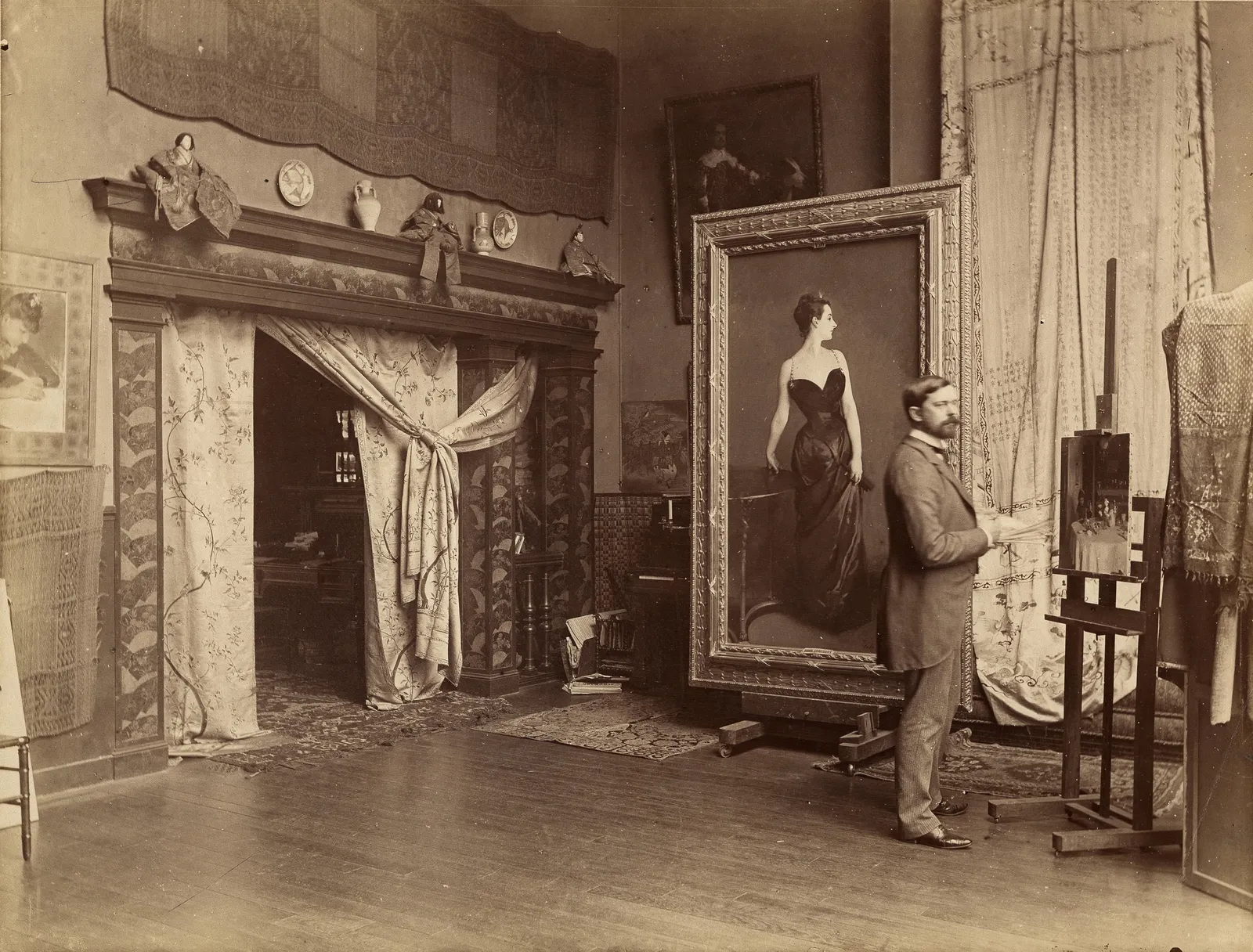 Sargent standing in his Paris studio in 1884, the portrait of Madame X on a rolling stand beside him and a working easel at the right. The room in front of the easel is bare floor for several paces, which is the distance he judged a canvas from.