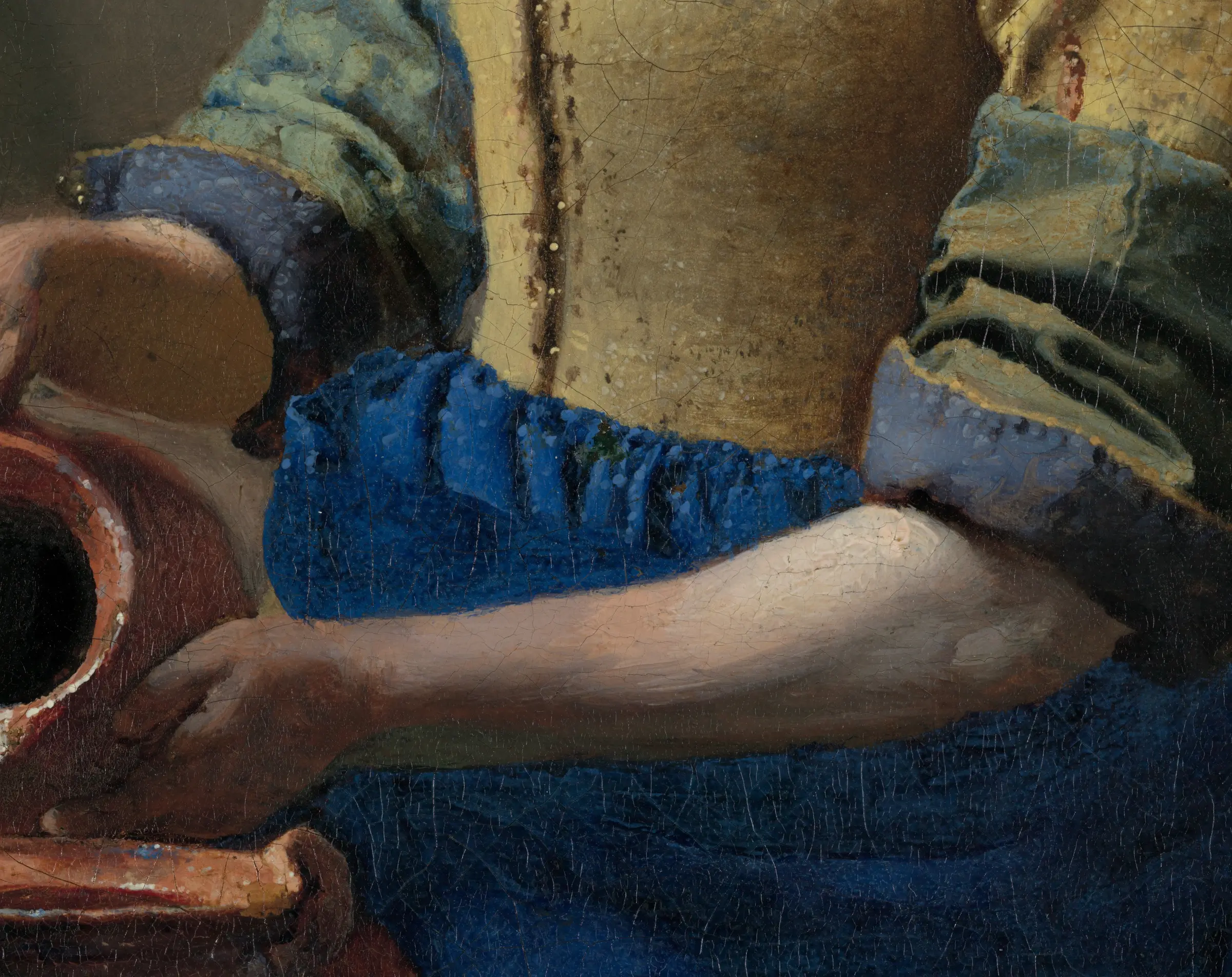 Detail of The Milkmaid at her lower arm: the blue sleeve and the bodice carry rows of small raised beads of paler paint, and the arm below them is one smooth run of warm light with almost no drawing in it. Under her left arm the 2022 scans found a thick line of black paint laid down fast, part of a rough underpainting the finished surface hides completely.