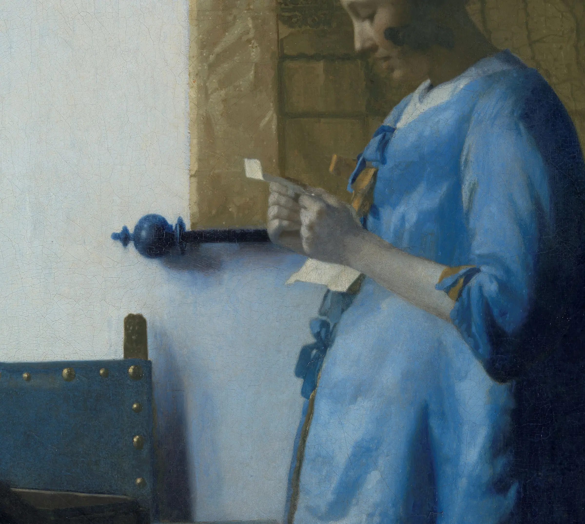 Detail of Woman Reading a Letter: the wall behind her is not white, it is a cool grey blue that lightens and warms where the window light lands. Her jacket is ultramarine and it meets that wall without one drawn edge anywhere. The map, the chair back and the curtain rod carry every hard line in the passage.